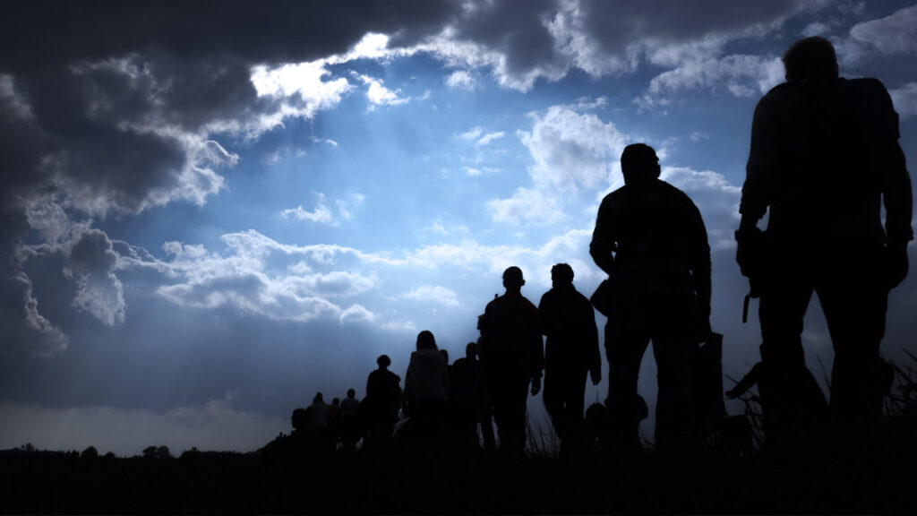 Grupo de personas caminan en una filta, en contraluz. Encuentra aquí la oración del migrante Santo Toribio Romo.