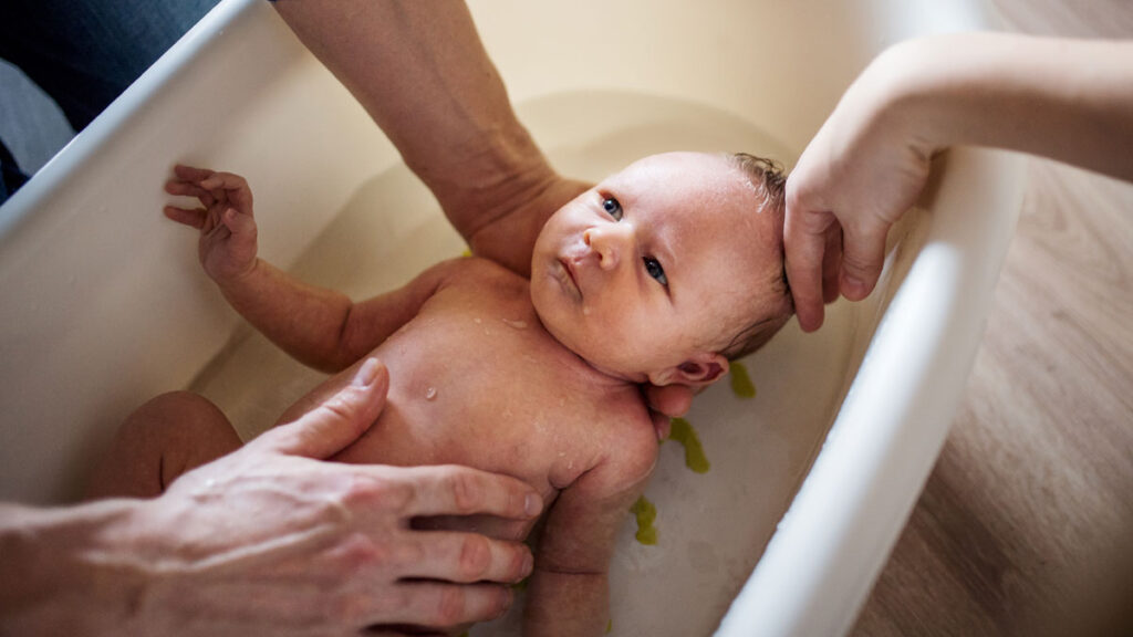 Manos lavan y bañar a un bebé recién nacido. Aprende a los cuántos días se baña un recién nacido.